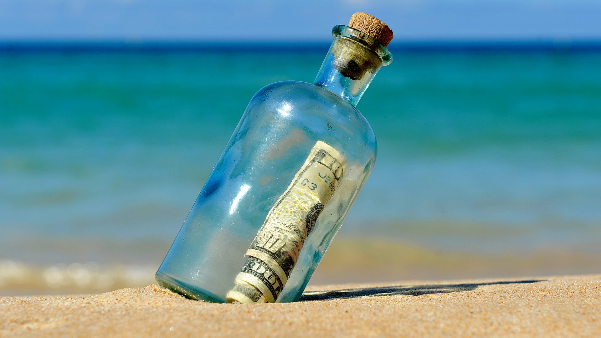 An image of a bottle with a banknote inside on the shore. Benefits of offshore banking