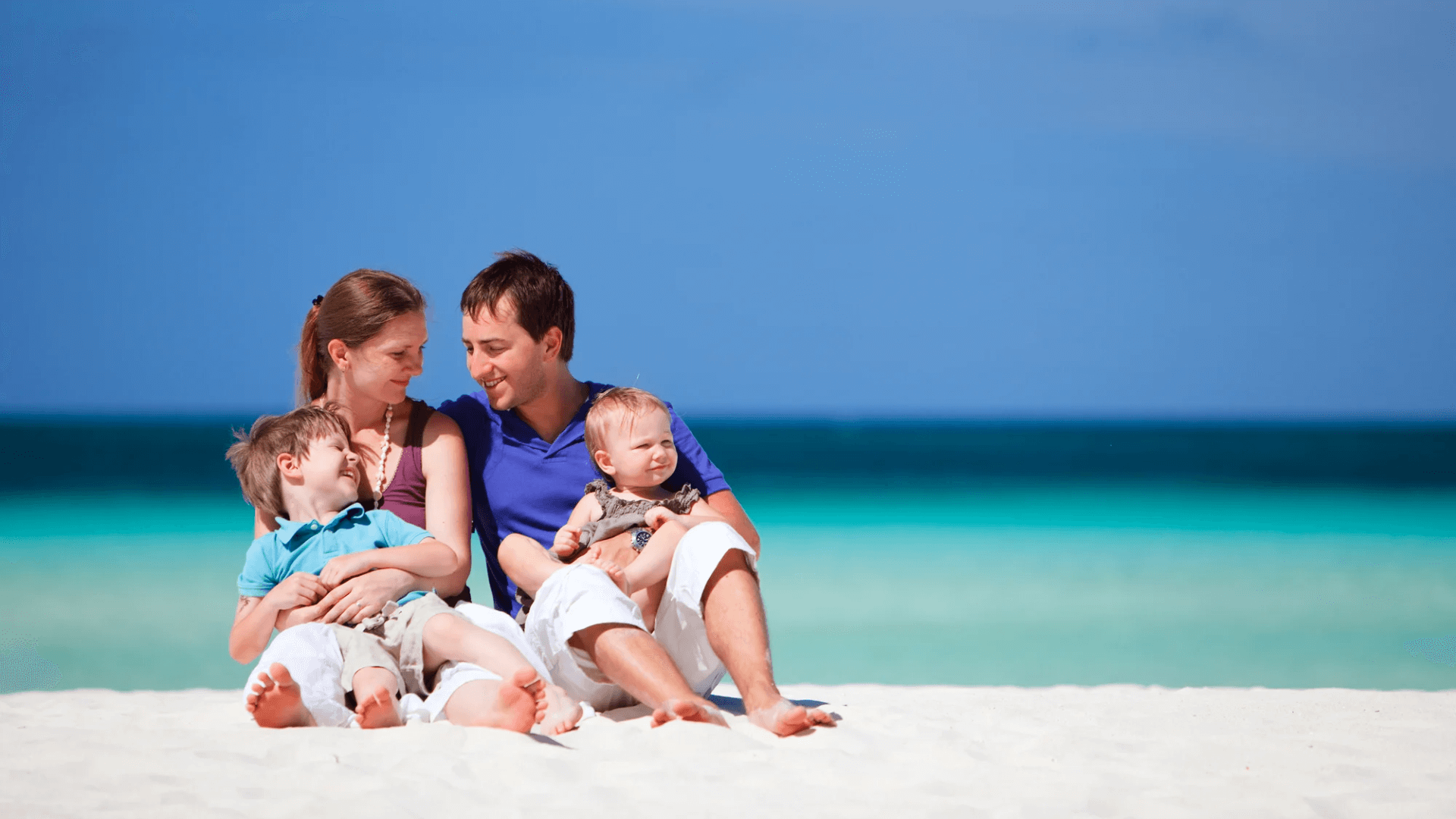 An image of a couple sat on the beach with two young children. life insurance for new parents
