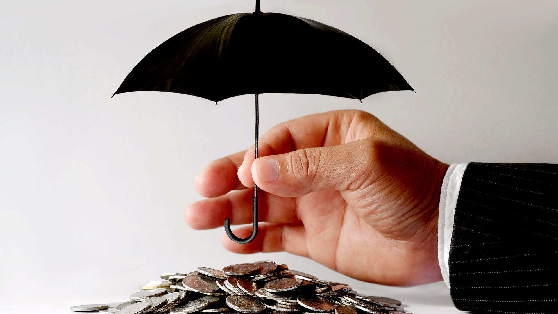 An image of a hand holding a small black umbrella. Underneath the umbrella there is a pile of coins. Income protection insurance for expats