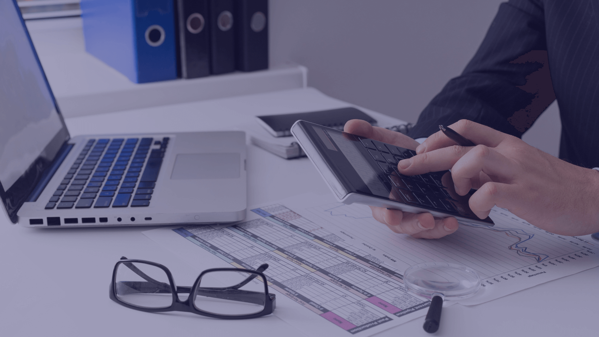 An image of a person using a calculator in front of a laptop. Free financial review